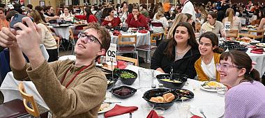 A student takes a selfie with the dinner participants in the background.